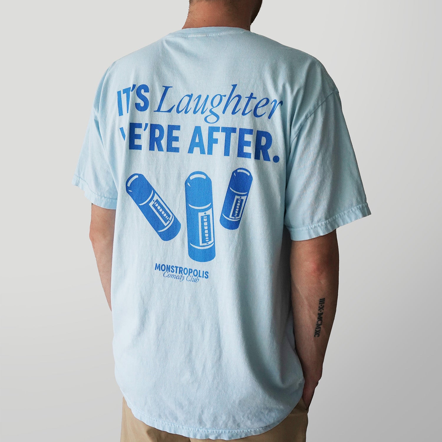Back view of a Disney-inspired Monstropolis Comedy Club t-shirt featuring the phrase ‘It’s Laughter We’re After’ above three laugh canisters with small Monstropolis Comedy Club text underneath.