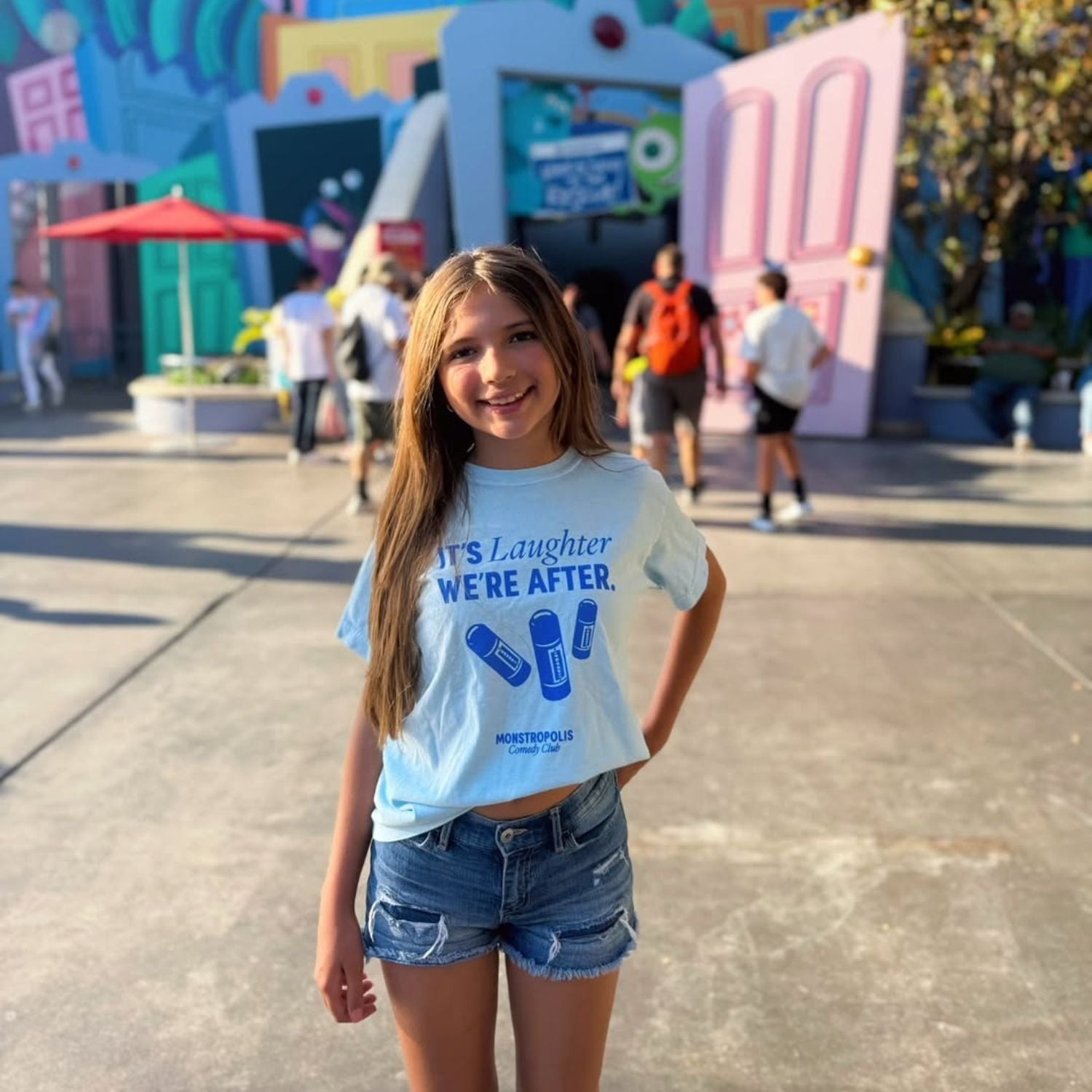 Child at Disney park wearing the Monstropolis Comedy Club t-shirt with ‘It’s Laughter We’re After’ and three laugh canisters printed on the front.