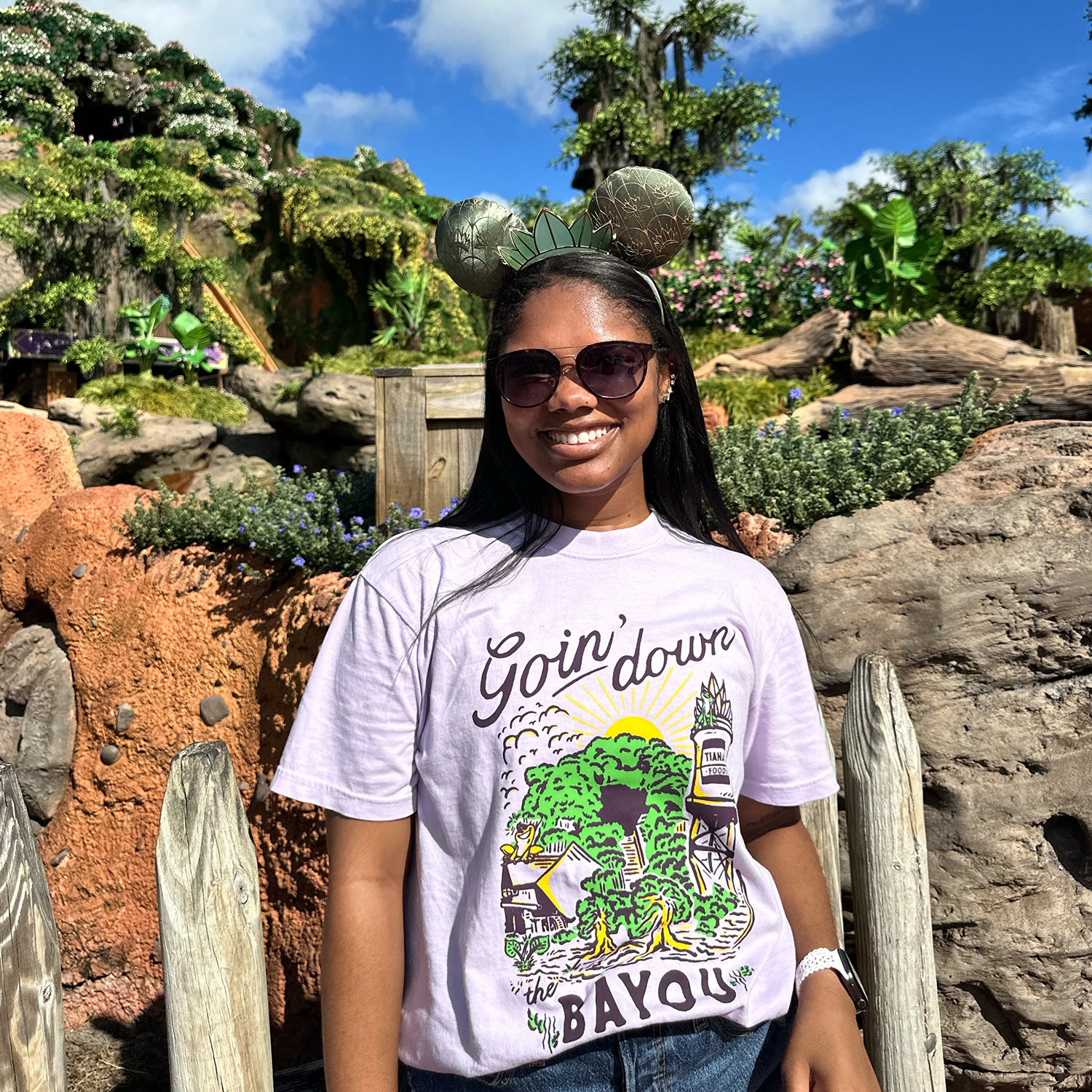 Front view of Disney-inspired Goin’ Down the Bayou t-shirt featuring text ‘Goin’ Down the Bayou’ above artwork of Tiana’s Bayou Adventure ride exterior with the big drop, Tiana’s Foods water tower, and cypress trees.
