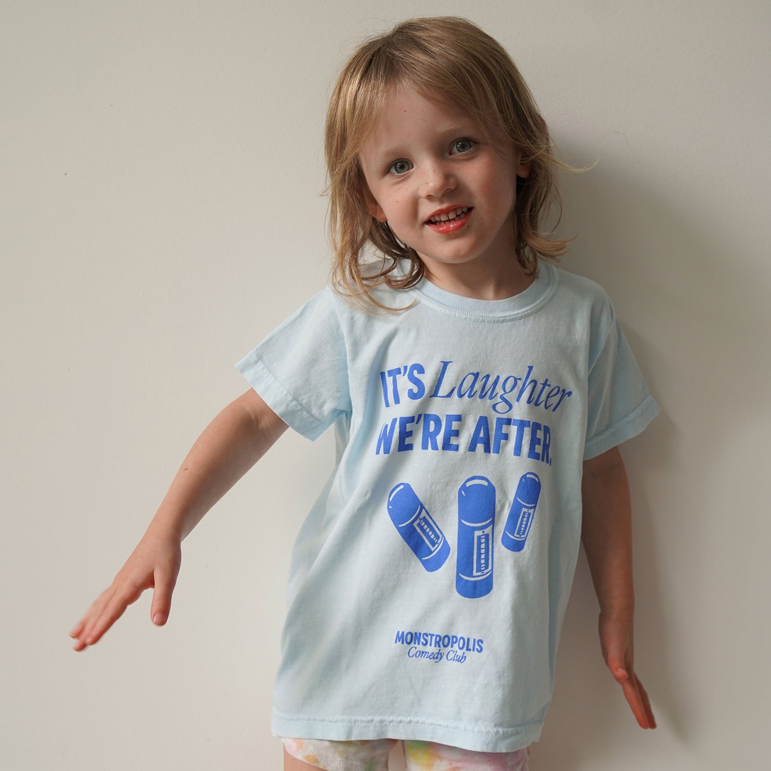 Front view of kids’ Disney-inspired Monstropolis Comedy Club t-shirt featuring the phrase ‘It’s Laughter We’re After’ above three laugh canisters with Monstropolis Comedy Club text underneath.