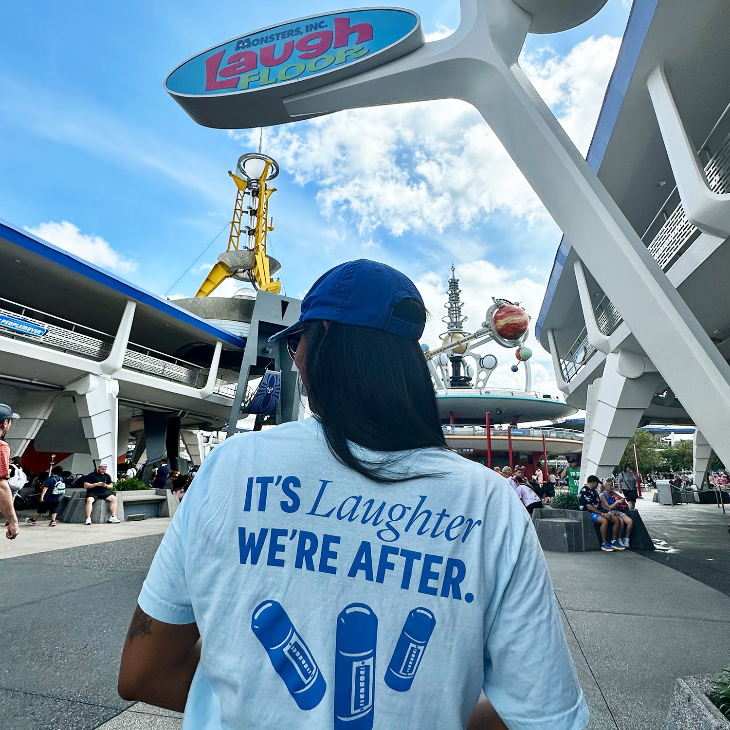 Woman at a Disney park wearing the Monstropolis Comedy Club t-shirt with ‘It’s Laughter We’re After’ and three laugh canisters on the back.