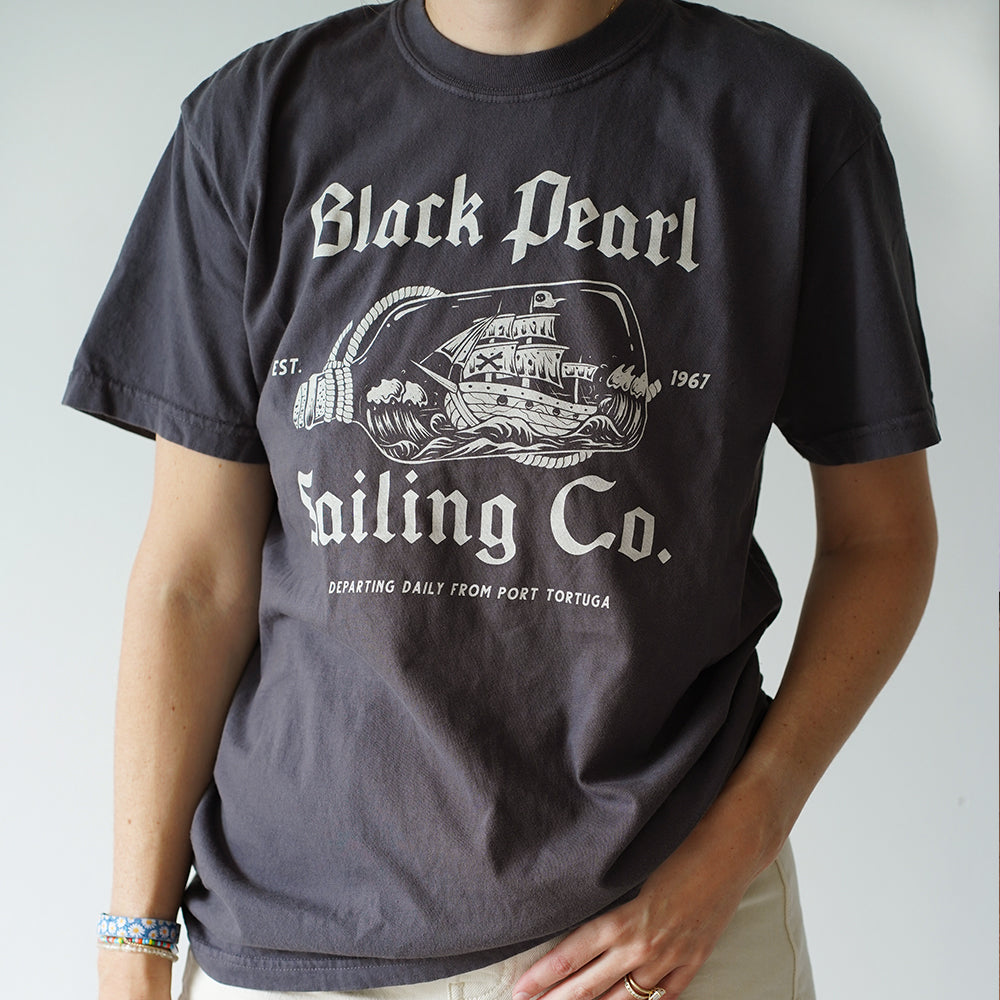 Front view of Disney-inspired Black Pearl Sailing Co. t-shirt featuring a ship-in-a-bottle design with the Black Pearl, small text ‘Est. 1967,’ and the phrase ‘Departing Daily From Port Tortuga.