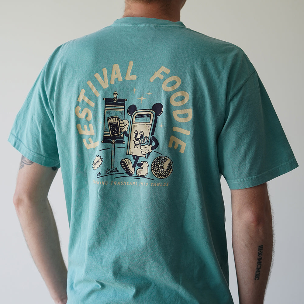 Back view of Disney-inspired Festival Foodie t-shirt with the phrase ‘Festival Foodie’ above a cartoon trash can with Mickey ears walking around the world, holding a beer and french fries, and smaller text reading ‘Turning Trashcans Into Tables.’