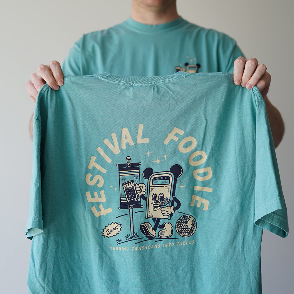 Back view of Disney-inspired Festival Foodie t-shirt with the phrase ‘Festival Foodie’ above a cartoon trash can with Mickey ears walking around the world, holding a beer and french fries, and smaller text reading ‘Turning Trashcans Into Tables.’