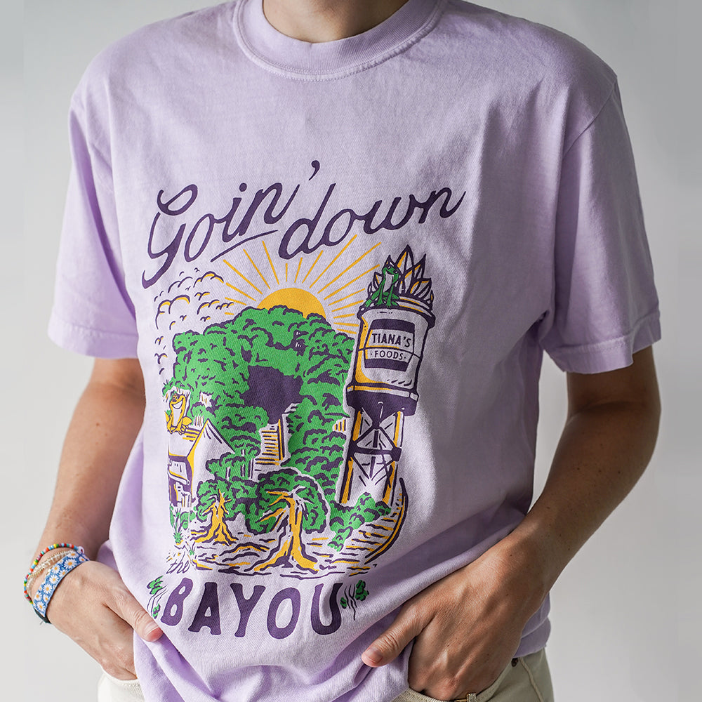 Front view of Disney-inspired Goin’ Down the Bayou t-shirt featuring text ‘Goin’ Down the Bayou’ above artwork of Tiana’s Bayou Adventure ride exterior with the big drop, Tiana’s Foods water tower, and cypress trees.