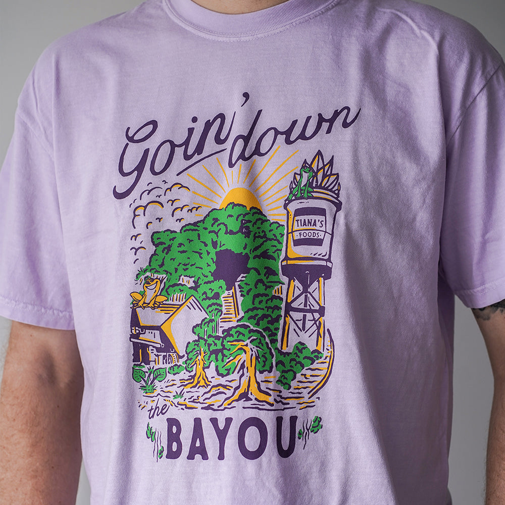Front view of Disney-inspired Goin’ Down the Bayou t-shirt featuring text ‘Goin’ Down the Bayou’ above artwork of Tiana’s Bayou Adventure ride exterior with the big drop, Tiana’s Foods water tower, and cypress trees.