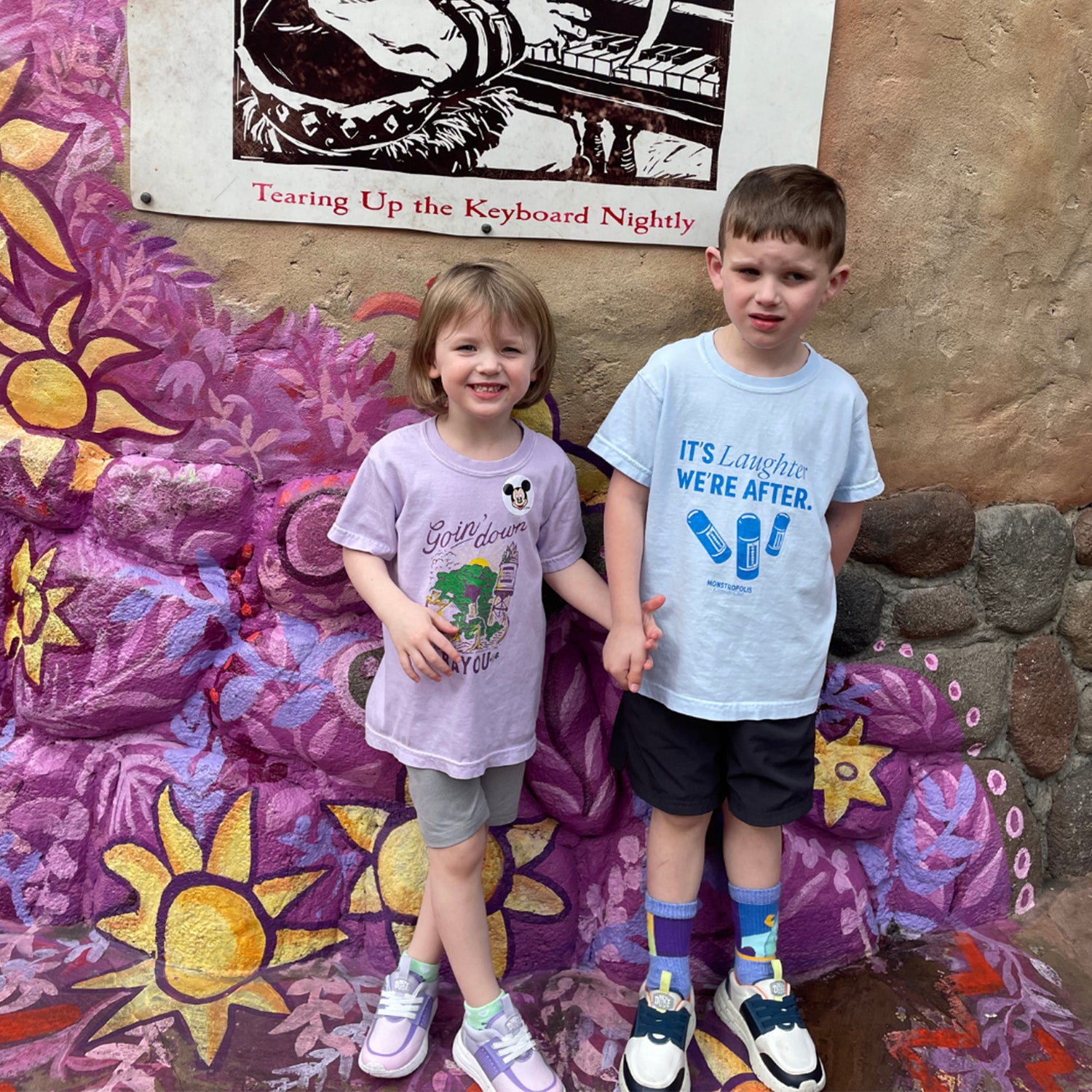 Front view of kids’ Disney-inspired Monstropolis Comedy Club t-shirt featuring the phrase ‘It’s Laughter We’re After’ above three laugh canisters with Monstropolis Comedy Club text underneath.