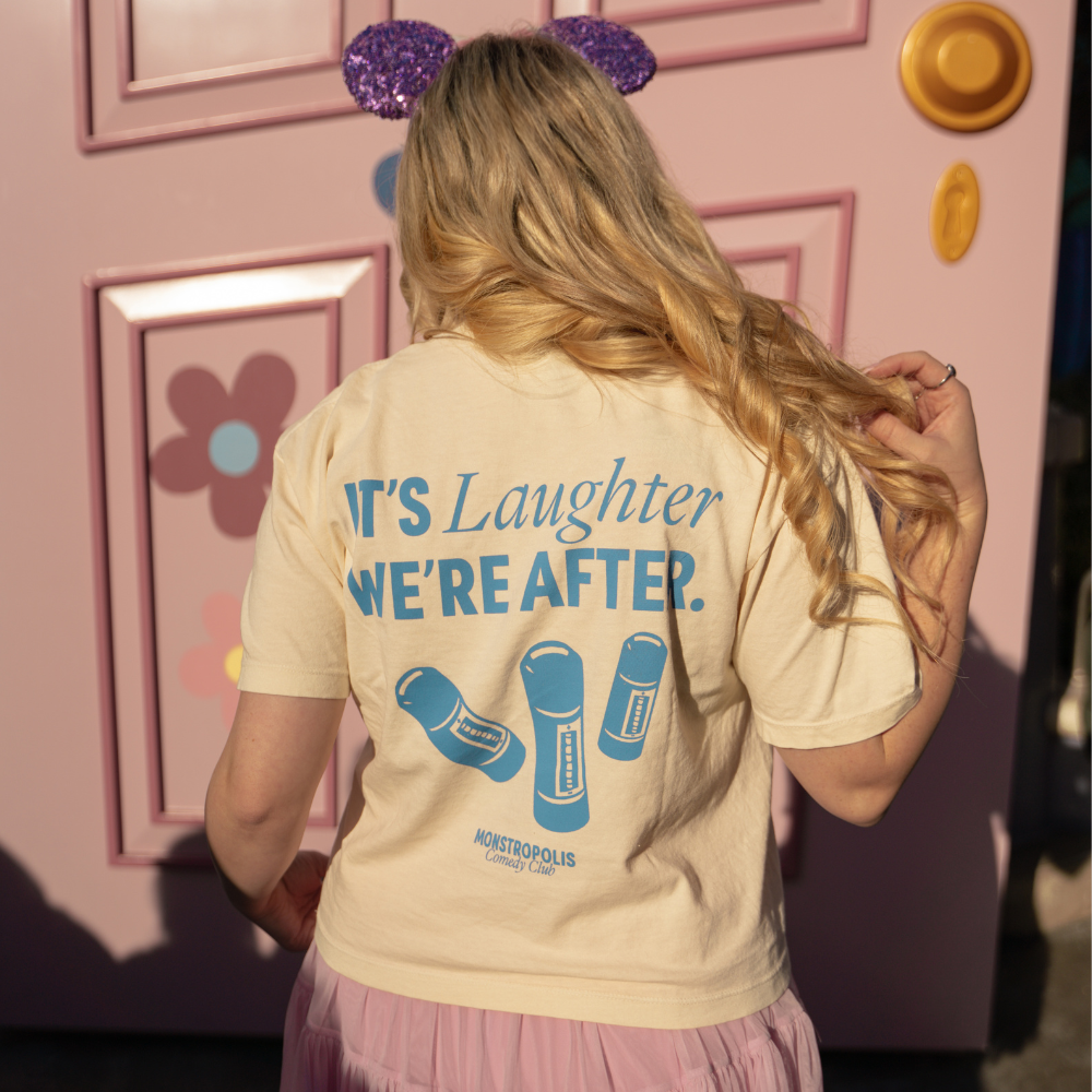 Back view of Disney-inspired Monstropolis Comedy Club crop top with the phrase ‘It’s Laughter We’re After’ above three laugh canisters and Monstropolis Comedy Club text underneath.