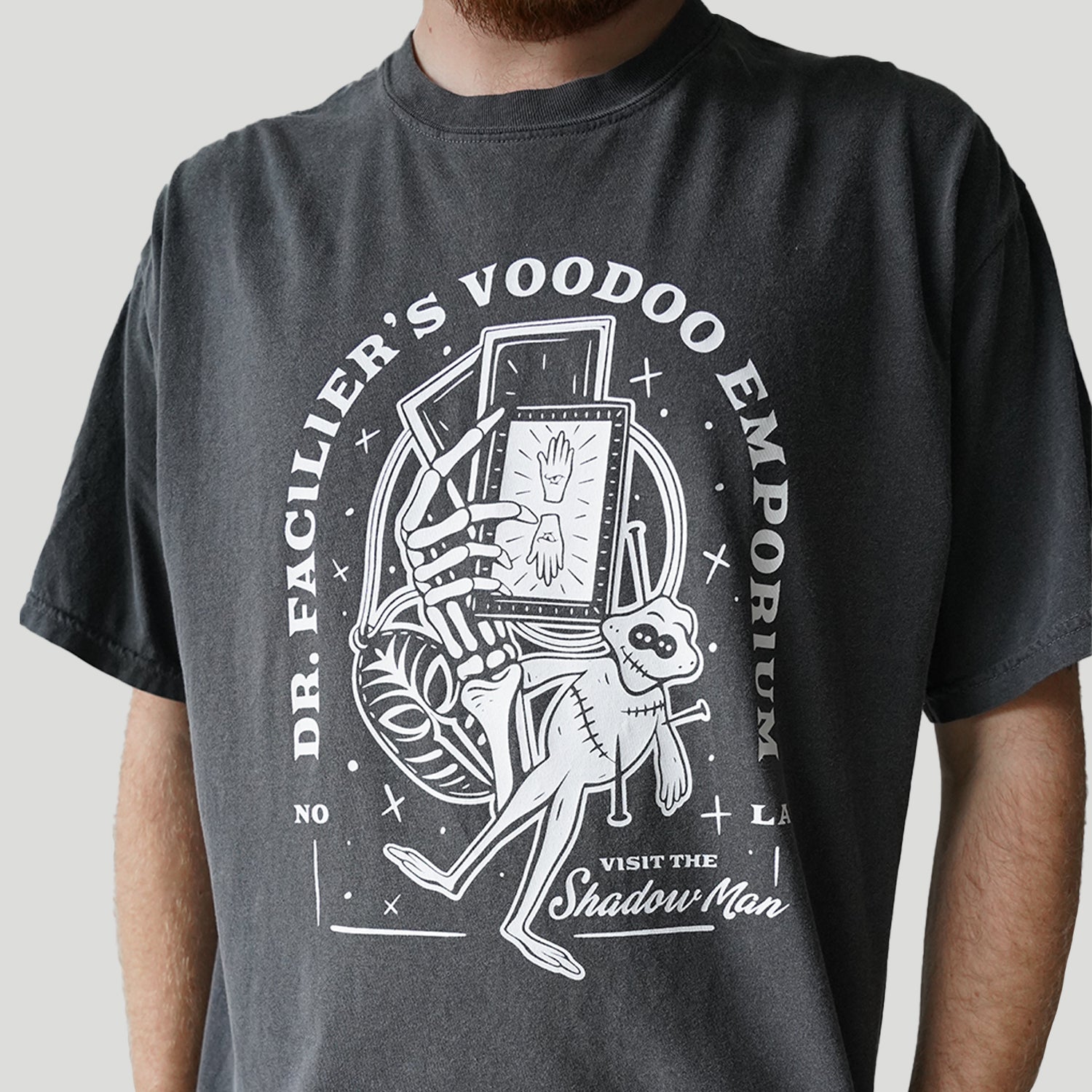 Front view of Disney-inspired Dr. Facilier’s Voodoo Emporium t-shirt with text ‘Dr. Facilier’s Voodoo Emporium,’ ‘NOLA,’ and ‘Visit the Shadow Man,’ featuring a voodoo frog and a skeleton hand holding playing cards.