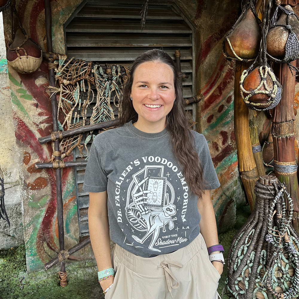 Front view of Disney-inspired Dr. Facilier’s Voodoo Emporium t-shirt with text ‘Dr. Facilier’s Voodoo Emporium,’ ‘NOLA,’ and ‘Visit the Shadow Man,’ featuring a voodoo frog and a skeleton hand holding playing cards.