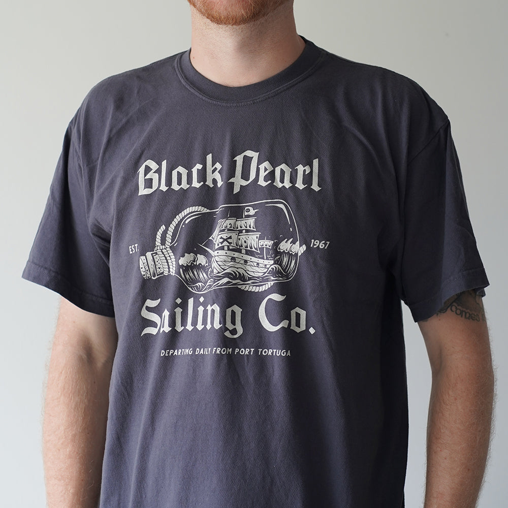 Front view of Disney-inspired Black Pearl Sailing Co. t-shirt featuring a ship-in-a-bottle design with the Black Pearl, small text ‘Est. 1967,’ and the phrase ‘Departing Daily From Port Tortuga.